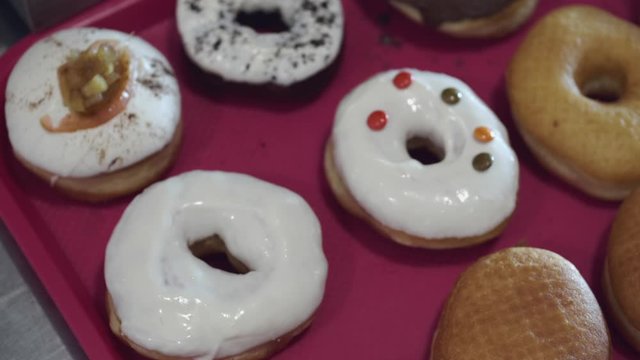 The baked donuts are being decorated by sweets. There are milky glaze and toppping on the donuts.