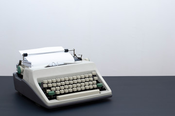 Old retro typewriter on a black wooden table against the background of a light wall.