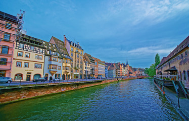 Strasbourg, France - April 30, 2012: Quay of Ill River with Spire of St Nicholas Church and Old Custom House in the old town of Strasbourg in Grand East region of France. People on the background