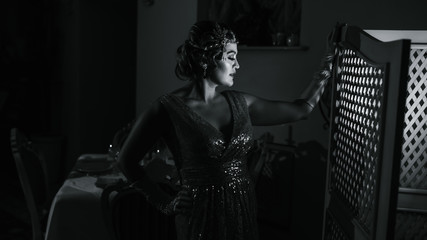 black and white photo with a woman with a diadem long gloves and a shiny dress standing at the...