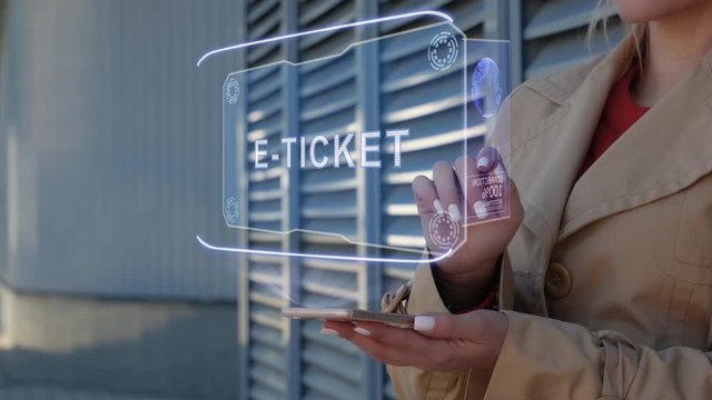 Unrecognizable businesswoman interacts HUD hologram with text E-ticket. Woman in the coat uses the technology of the future mobile screen on the background of the city
