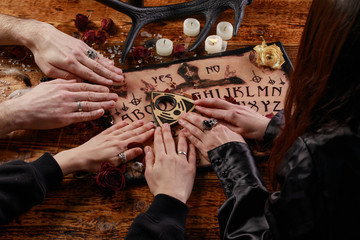 People conducting a seance using a Ouija Board, or Talking Spirit Board, with white candles. Shot...