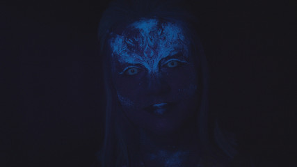 Woman with a glowing blue face looks at the camera 