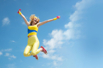 Young sporty excited girl jumping happily with hands up on sky background outdoor, panorama, copy space, sunrise light. Fashion and Trends in Sport. Health and fitness. Daily workout outdoors.
