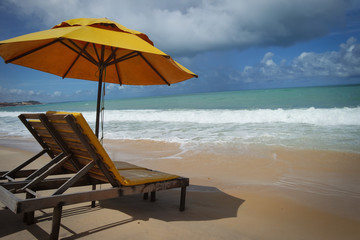 big yellow beach umbrella with chairs  at a cloudy but still sunny beach