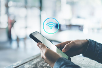 Woman hand using smartphone with wifi icon in cafe shop background.