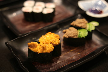 Uni sushi roe gunkanmaki. assorted Japanese sushi on wood plate platter on dark wooden table.