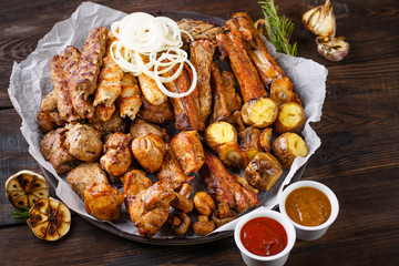 Assorted delicious grilled meat and vegetables with bbq sauces on plate on wooden background. Big set of hot meat dishes, grill and barbeque, restaurant menu