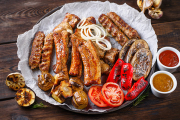 Assorted delicious grilled meat and vegetables with bbq sauces on plate on wooden background. Big set of hot meat dishes, grill and barbeque, restaurant menu
