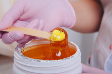 Wax for depilation close-up. girl pulls out cosmetic product from jar. Hand with wooden stick for cosmetic procedures. Sugaring: epilation with liquate sugar at legs
