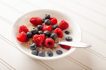 White bowl of cracked wheat cereal topped with blueberries, raspberries, and milk