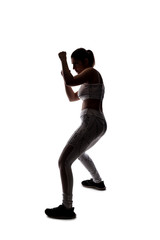 Fit young woman in a fighting stance wearing athletic sports wear and exercising by punching or practicing self defense.  She is backlit as a silhouette on a white background