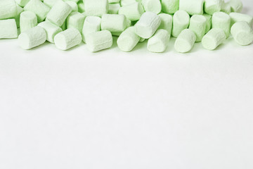 Sweet green mini marshmallows on white paper background with copy space. Selective focus.