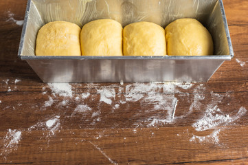 Yellow bread dough in a metal baking tin with flour dusting on wood texture table surface.