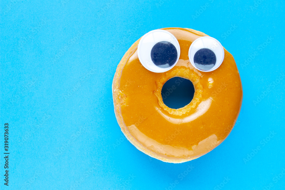 Wall mural a canadian maple dip donut with black wiggle googly eyeballs on a blue background