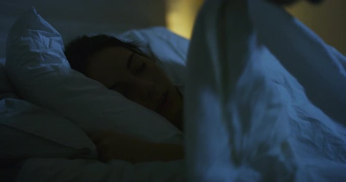 Authentic shot of tender husband is covering with a blanket and giving a kiss to his wife while sleeping in a bed at night. Shot in 8K. Concept of wellbeing, healthcare, lifestyle,bedding, love, care