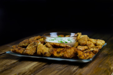 Chicken nuggets. Breaded meat snacks. Crispy fried crust. Fast food. High-calorie foods on a wooden table. White sauce for dipping meat pieces.