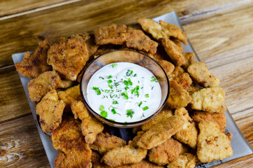 Chicken nuggets. Breaded meat snacks. Crispy fried crust. Fast food. High-calorie foods on a wooden table. White sauce for dipping meat pieces.
