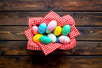 Basket with painted eggs for Easter dinner on dark wooden desk top-down copy space