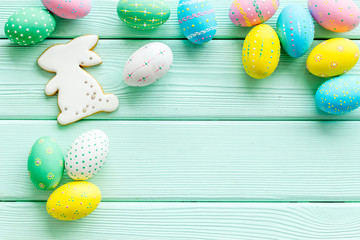 Easter symbols. Painted eggs and bunny gingerbread on green wooden desk top-down frame copy space