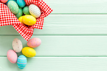 Easter eggs painted in basket on green wooden desk top-down copy space