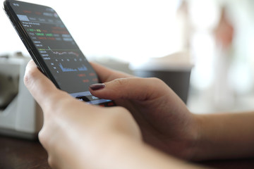 Female hand with smartphone trading stock online in coffee shop , Business concept