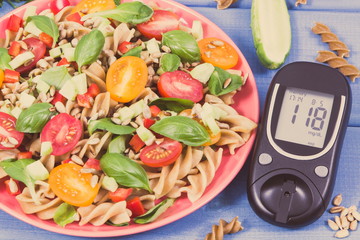 Glucometer with sugar level and salad with wholegrain pasta and vegetables. Diabetes, dieting and...