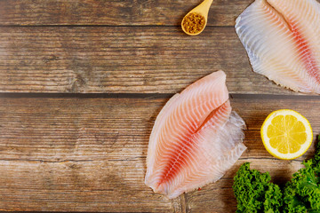 Pink tilapia with lemon and spices on wooden background.