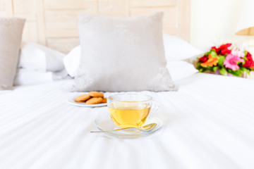 Fototapeta na wymiar Herbal tea on bed linen in the upscale hotel room. Being alone, getaway, staycation, digital detox concepts. Horizontal
