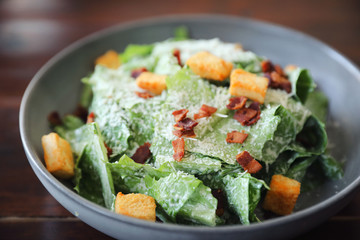 Caesar salad with crispy bread and bacon close up on wood background
