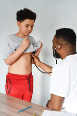 An african american doctor with his mixed preteen male. A cute black paediatrician examining his young mixed preteen boy patient with a stethoscope.
