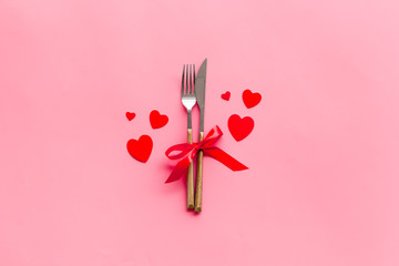 Valentines' Day dating in restaurant concept. Fork and knife decorated with hearts on pink...