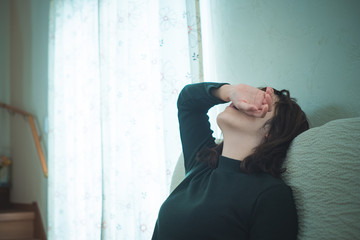 ソファでぐったりする女性　頭痛　疲労　子育て　生理痛
