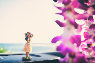 Hula car dashboard road trip Hawaii dancer doll - girl dancing on summer holiday vacation in Maui. with purple fresh flower lei hanging from mirror.