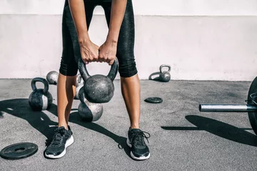 Rolgordijnen Kettlebell Gewichtheffen atleet vrouw tillen gewicht op outdoor fitness gym. Onderlichaam benen en voeten close-up van krachttraining benen, bilspieren en rug opheffing van vrije gewichten. © Maridav