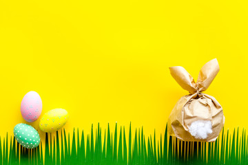 Easter symbols. Bunny and painted eggs on grass on yellow background top-down frame copy space