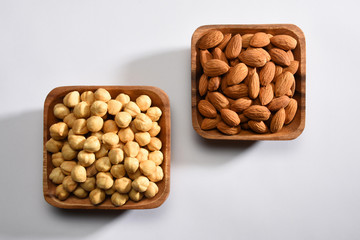 Hazelnuts and almonds in the wooden bowls on white background