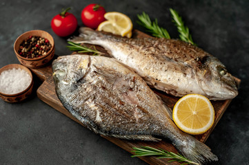 grilled dorado fish on a cutting board with spices and lemon on a stone background