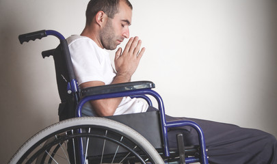 Disabled man in wheelchair praying in home.