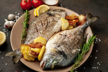 grilled dorado fish and fried potatoes on a plate with spices and lemon on a stone background