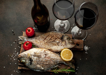 dinner for two - grilled dorado fish served on a cutting board with spices and a bottle of wine, glasses on a stone background 