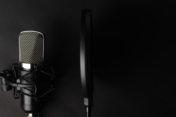 Black studio microphone on a black background with a pop filter with space for design