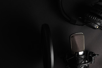 Flat lay, Studio microphone with pop filter and professional headphones. Black on a black background. Podcasts, radio, streams