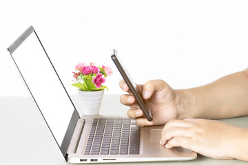 Mockup image of hands holding blank mobile phone while using laptop with blank white desktop screen.