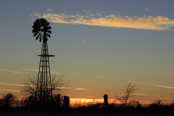 sunset in the field with a Windmill silhouette and fence in Kansas north of Hutchinson Kansas USA.