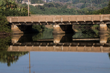 Fototapeta na wymiar Bridge Surrounded by Vegetation Reflecting in River
