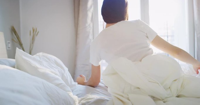 A healthy young woman is waking up after sleeping well with a sun beams in her bedroom in a morning. Shot in 8K. Concept of wellbeing, healthcare, lifestyle,bedding, happiness
