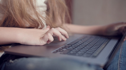 Closeup shallow depth of field of a little girl's hand on a laptop keyboard. The concept of using the younger generation of gadgets