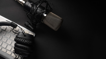 Flat lay, Studio microphone with professional headphones on a PC keyboard. Black on a black background. Podcasts, radio, streams, blogging, working with sound, recording tracks - obrazy, fototapety, plakaty