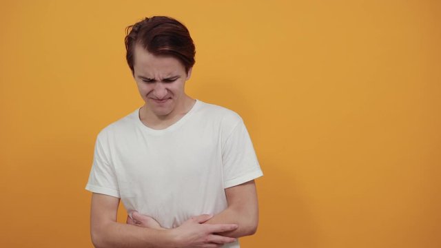 Stomach pains stomach problems white T-shirt young male on yellow background